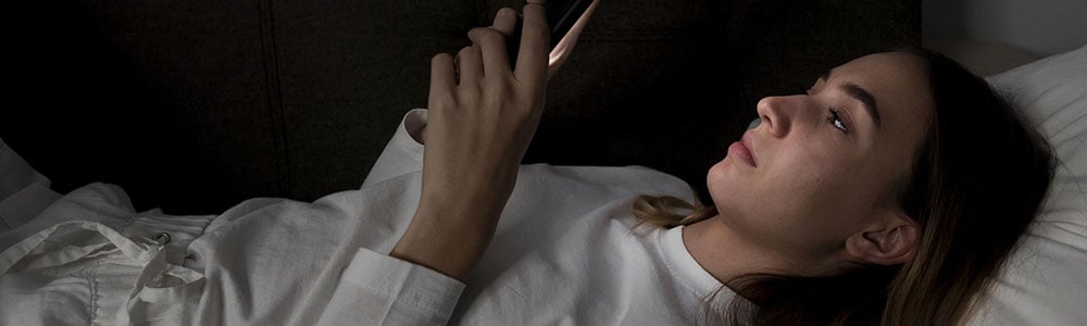 femme dans son lit regardant son téléphone mobile